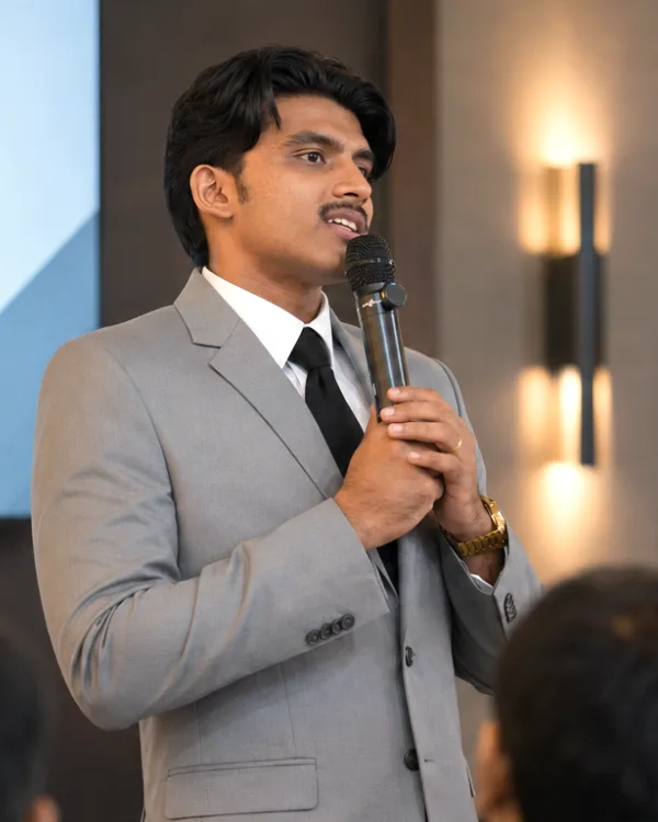 Jonah Joy in a grey suit speaking into a microphone to a seated room